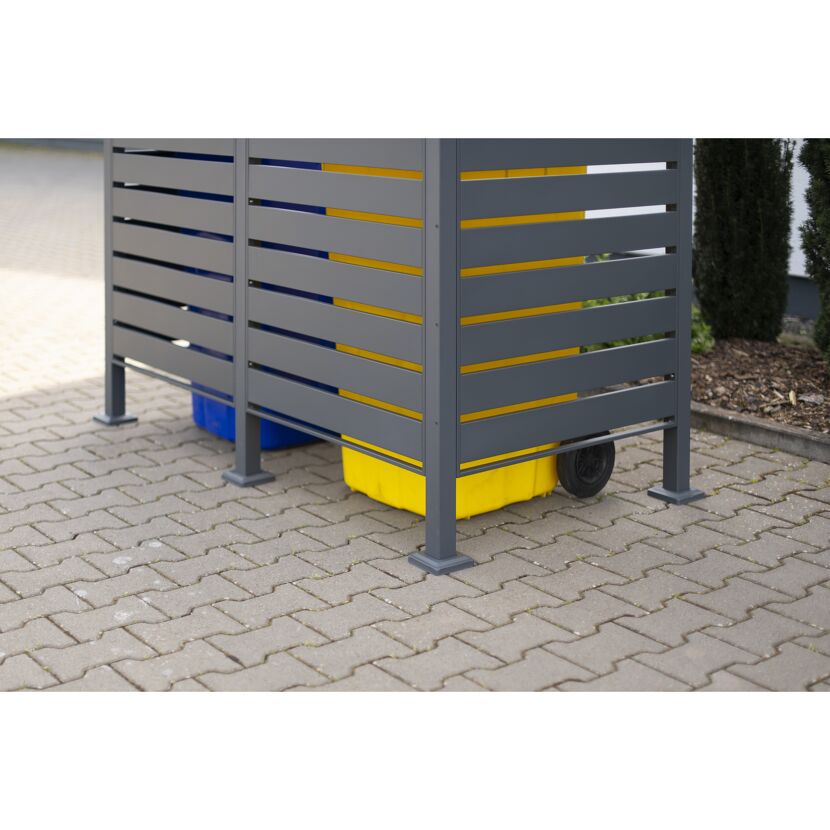 Gelbe und blaue Mülltonnen hinter einer grauen Mülltonnenverkleidung