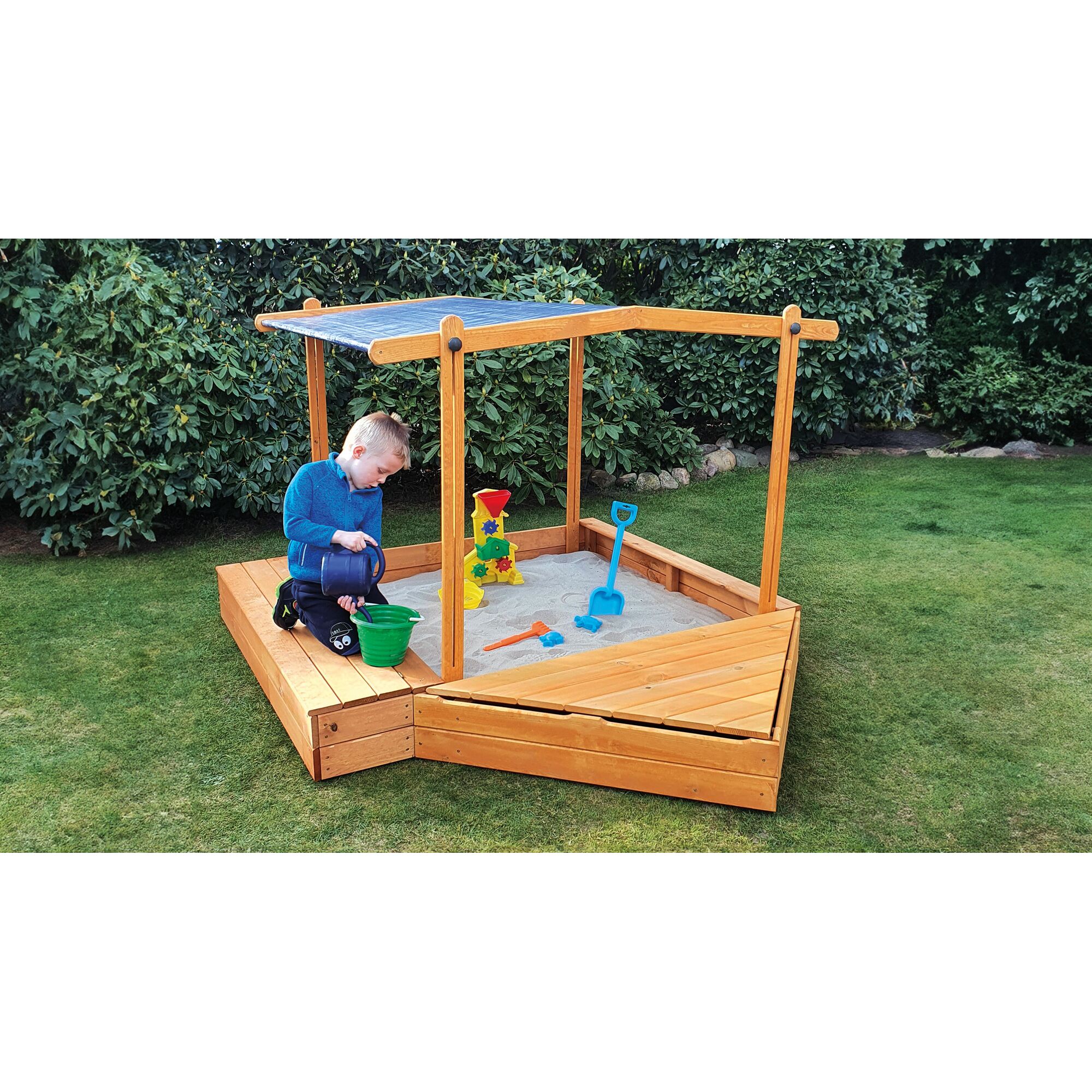 Kind spielt mit Gießkanne im Sandkasten mit Dach