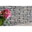 Graue Steinmauer mit unscharfer rosa Blume im Vordergrund