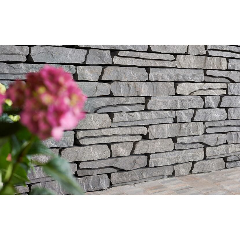 Graue Steinmauer mit unscharfer rosa Blume im Vordergrund