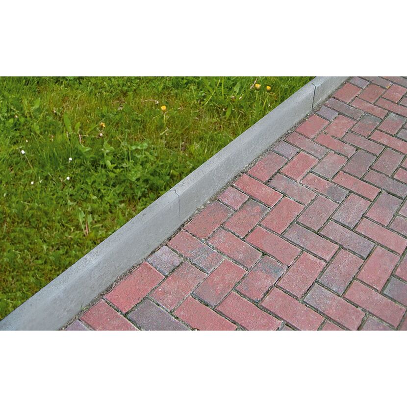 Graue Rasenkante neben rotem Pflastersteinweg.