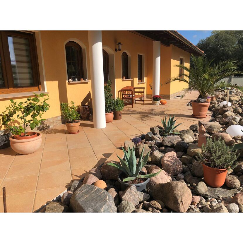 Eingangsbereich eines Hauses mit Terrakottafliesen, bepflanzten Töpfen und Steinen.