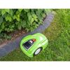 Grüner Rasenmähroboter mäht Rasen neben Beet