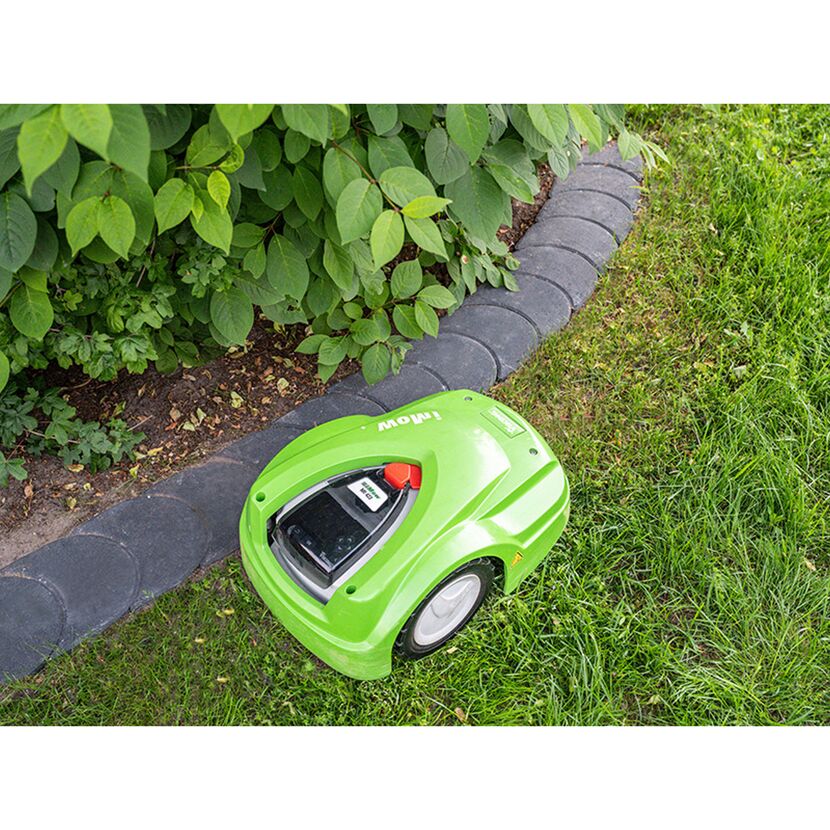 Grüner Rasenmähroboter mäht Rasen neben Beet