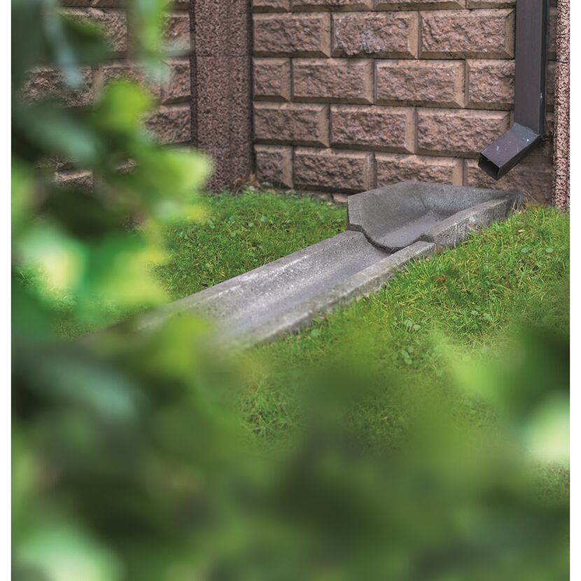Graue Ablaufrinne neben Hauswand im Garten