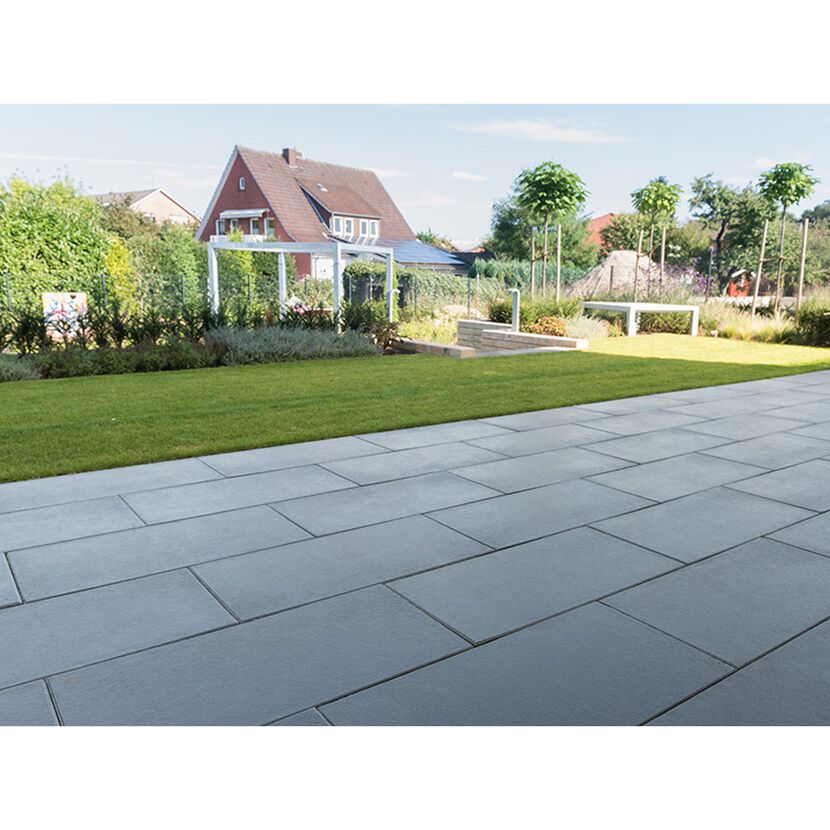 Gepflasterte Terrasse mit Rasenfläche und Haus im Hintergrund