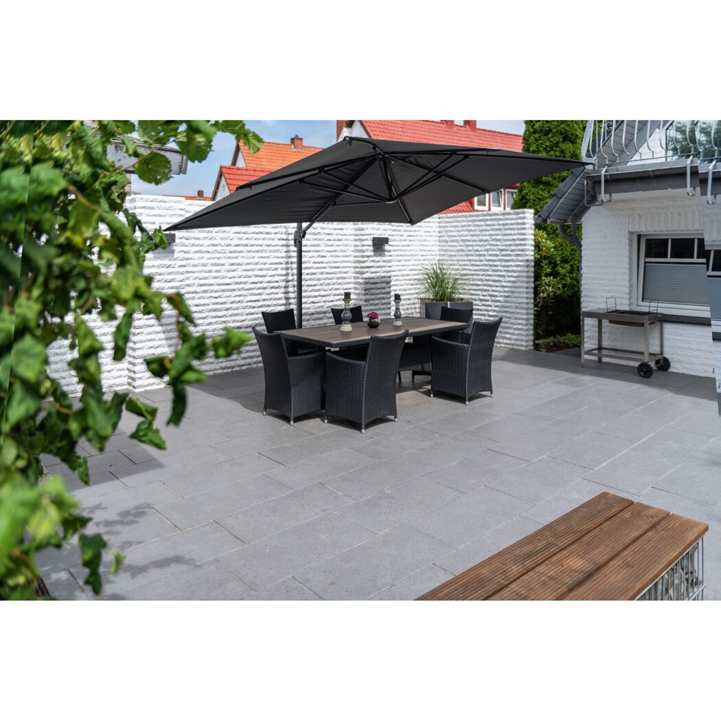Gepflasterte Terrasse mit Esstisch und Sonnenschirm.