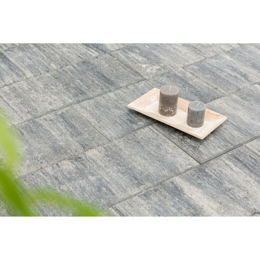 Zwei graue Stumpenkerzen auf einem Holztablett auf grauen Terrassenplatten