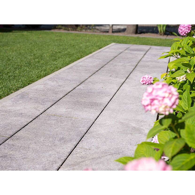 Graue Gehwegplatten im Garten neben Rasenfläche und Blumen