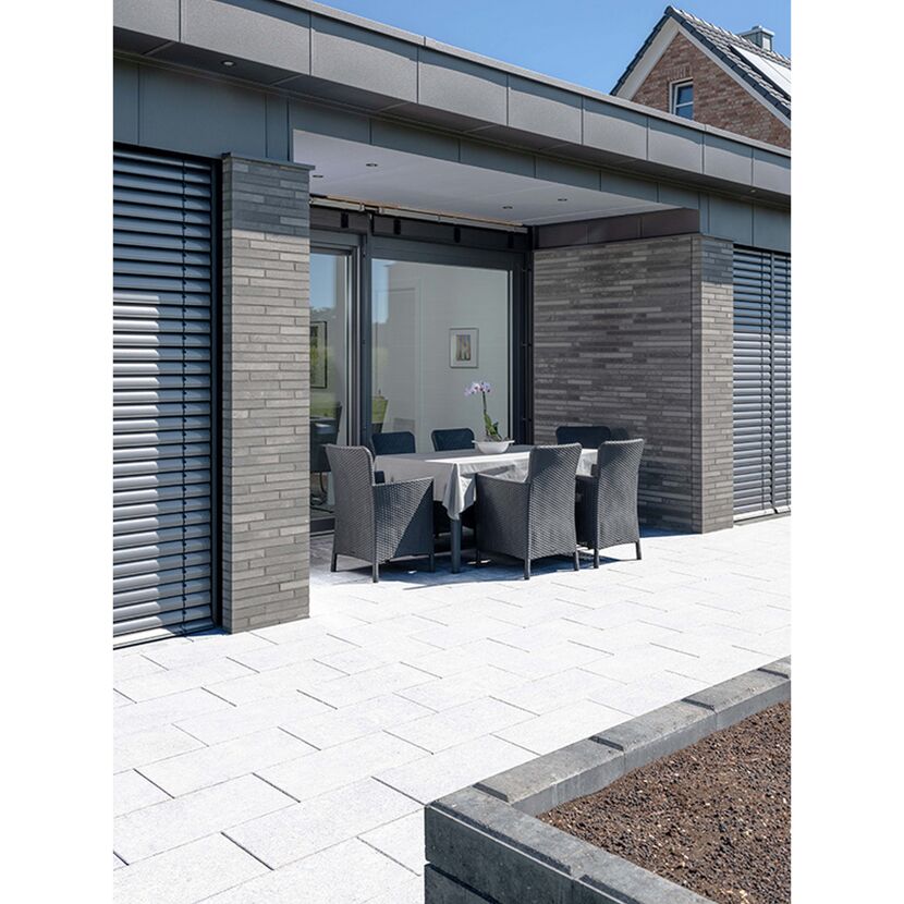 Gepflasterte Terrasse mit Esstisch und Stühlen.