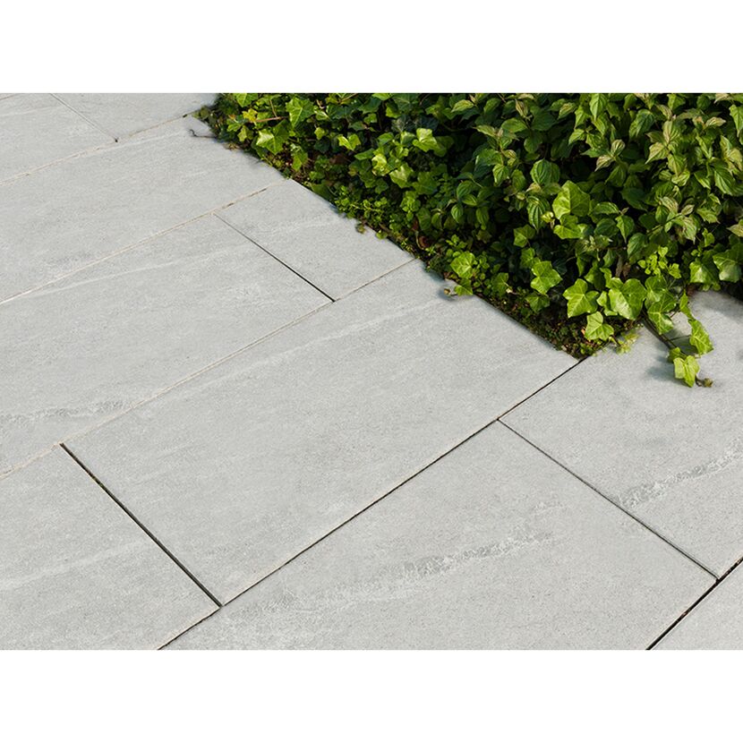 Graue Terrassenplatten neben grünen Pflanzen.
