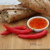 Chilischoten, Chilisauce und Brot auf einem Holzbrett