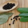 Schwarze Pfefferkörner in einem Holzlöffel und Lorbeerblätter