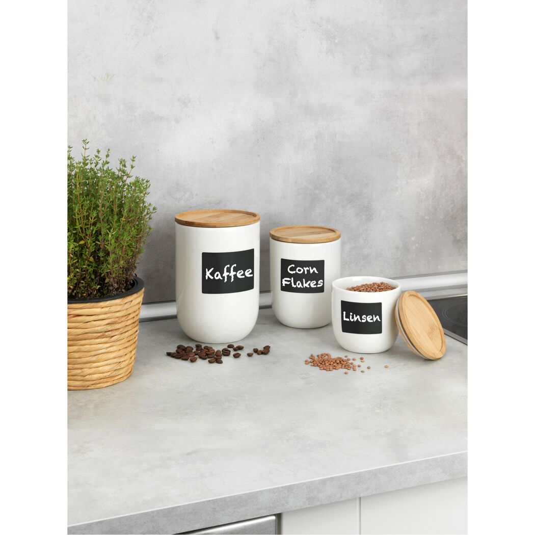 Drei weiße Vorratsdosen mit Bambusdeckeln für Kaffee, Cornflakes und Linsen.