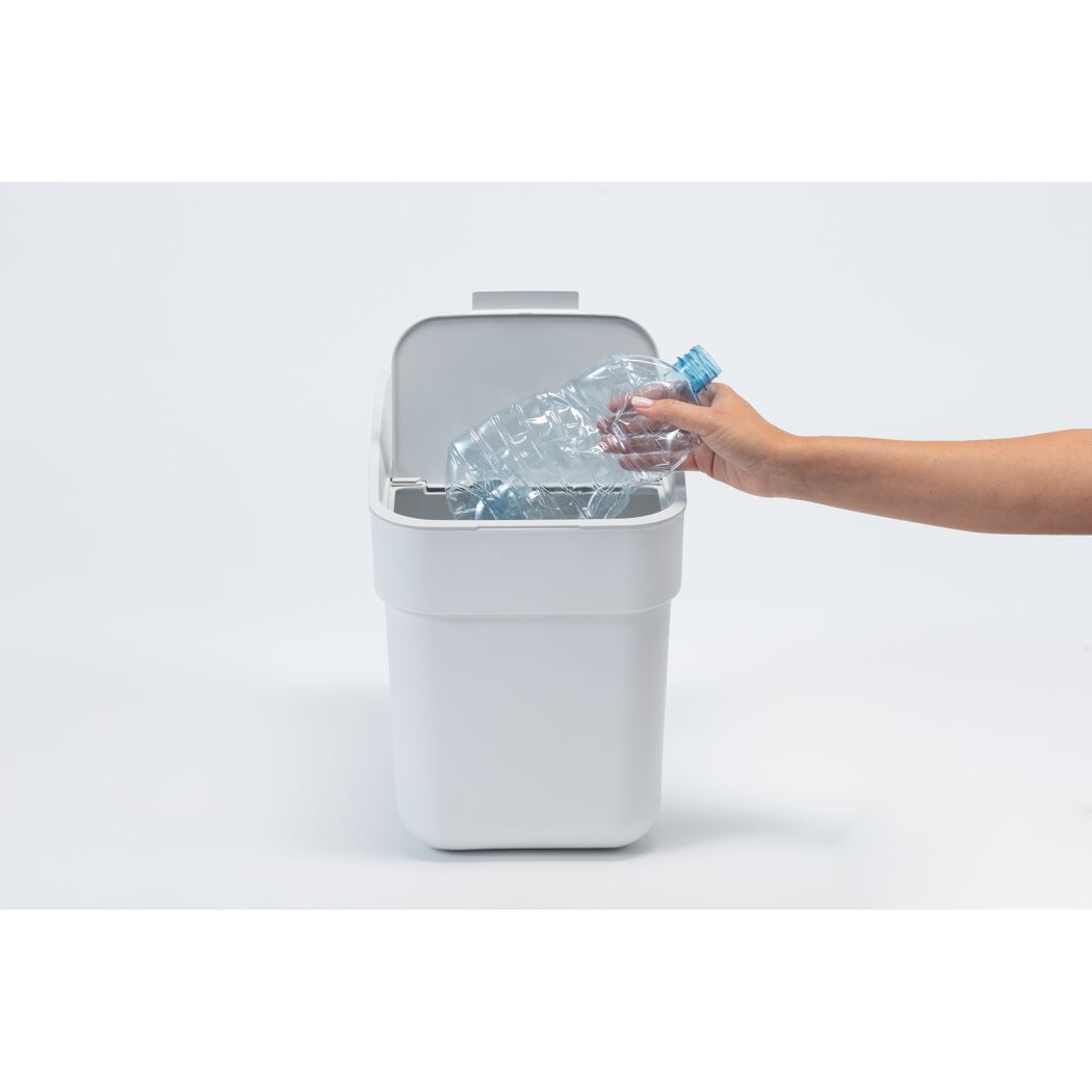 Hand wirft Plastikflasche in weißen Abfalleimer