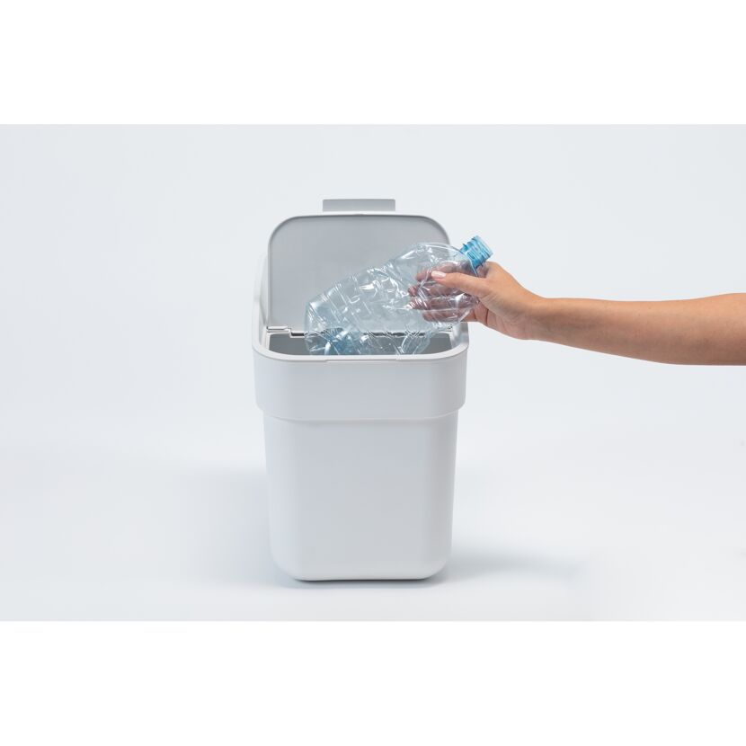Hand wirft Plastikflasche in weißen Abfalleimer