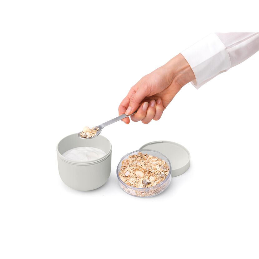 Person gibt Müsli mit einem Löffel in Joghurt