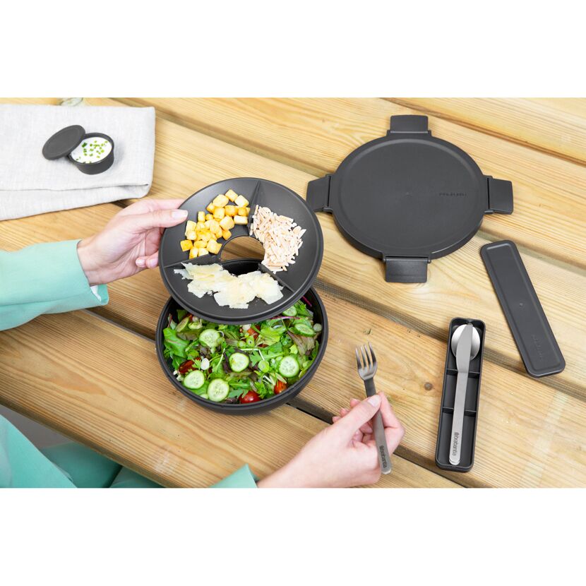 Person öffnet Lunchbox mit Salat, Gabel und Messer