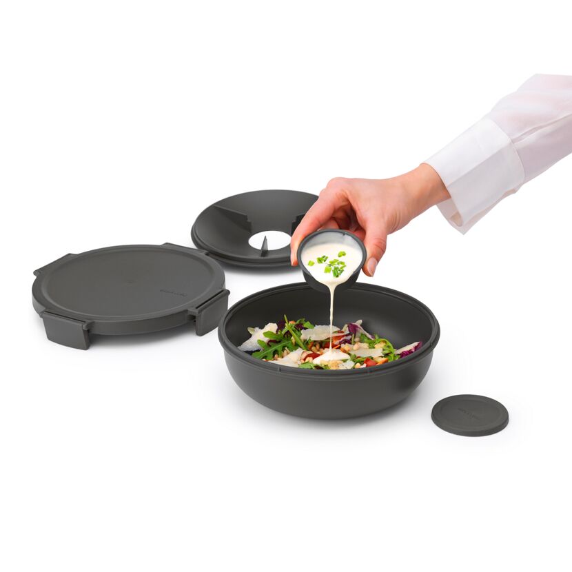 Person gibt Dressing über Salat in dunkle Salatschüssel