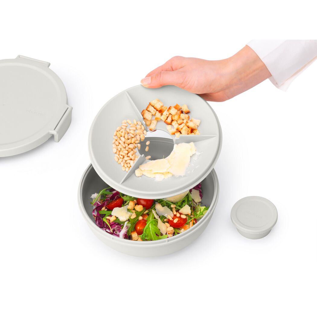 Person hält einen Salatschüssel-Deckel mit drei Fächern über einer Salatschüssel.