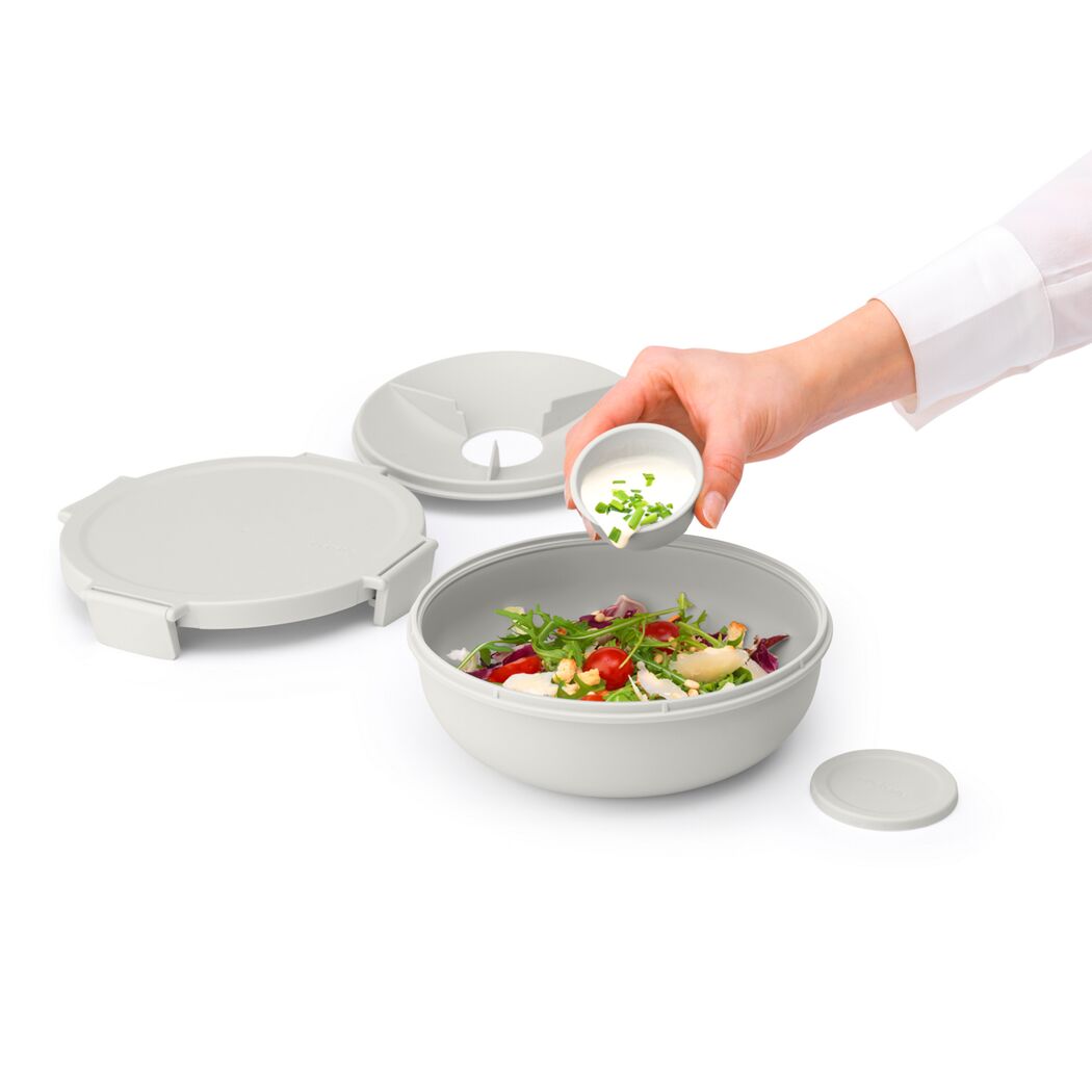 Person gibt Dressing über einen Salat in einer Salatschüssel