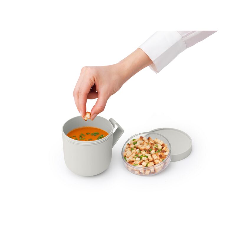 Person gibt Croutons in eine Tasse Suppe.