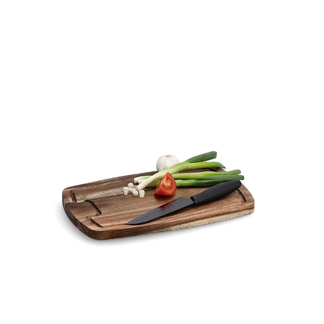Schneidebrett mit Frühlingszwiebeln, Knoblauch und Tomate. Ein Messer liegt daneben.