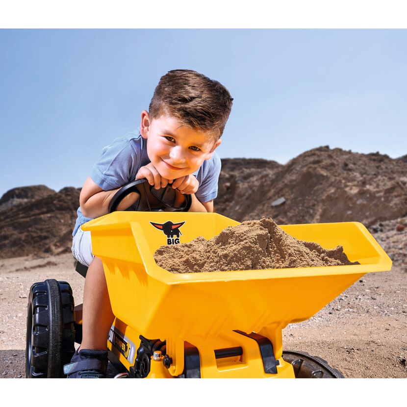 Kind mit Spielzeug-Kipplaster im Sand