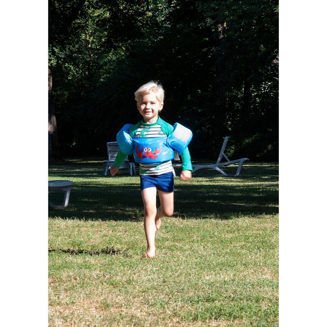 Kleinkind mit Schwimmflügeln rennt über eine Wiese.