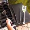 Person reinigt einen Grillrost mit einer Grillbürste.