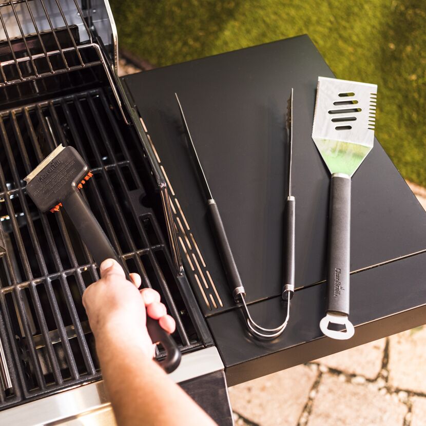 Person reinigt einen Grillrost mit einer Grillbürste.