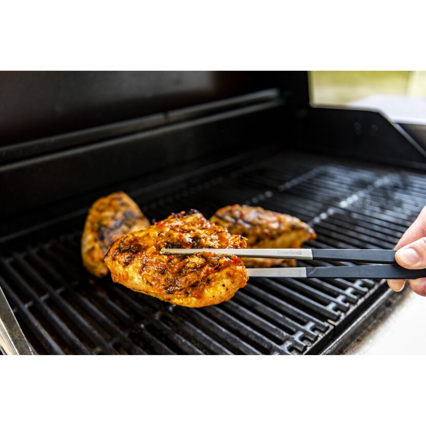 Hähnchen wird mit einer Grillzange gewendet
