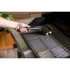 Person reinigt einen Grillrost mit einer Grillbürste.