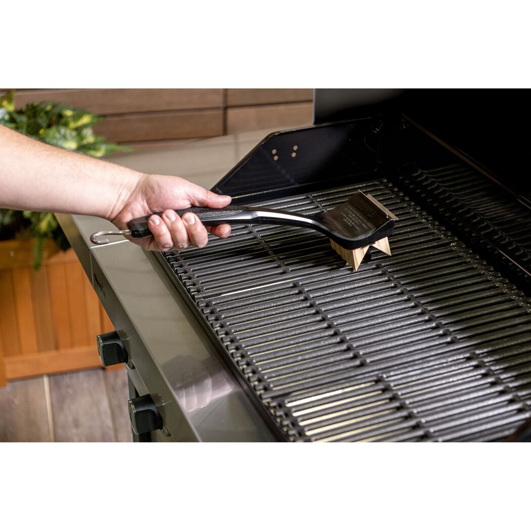 Person reinigt einen Grillrost mit einer Grillbürste.