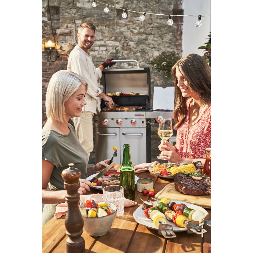 Drei Personen grillen und essen im Garten.