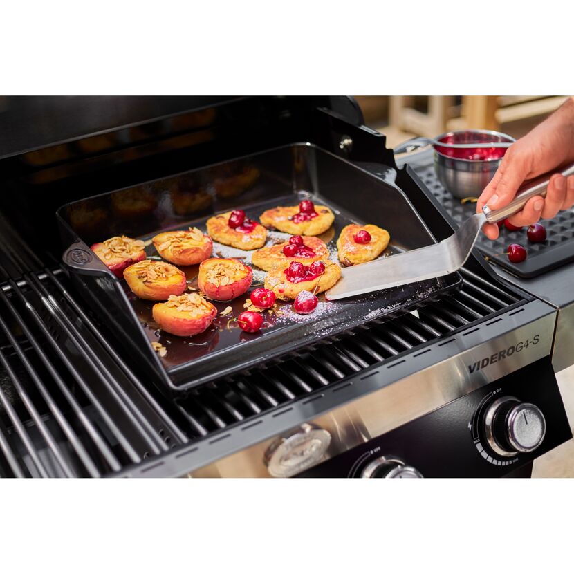 Person wendet Pfannkuchen und Pfirsiche mit einem Pfannenwender auf einem Grill.