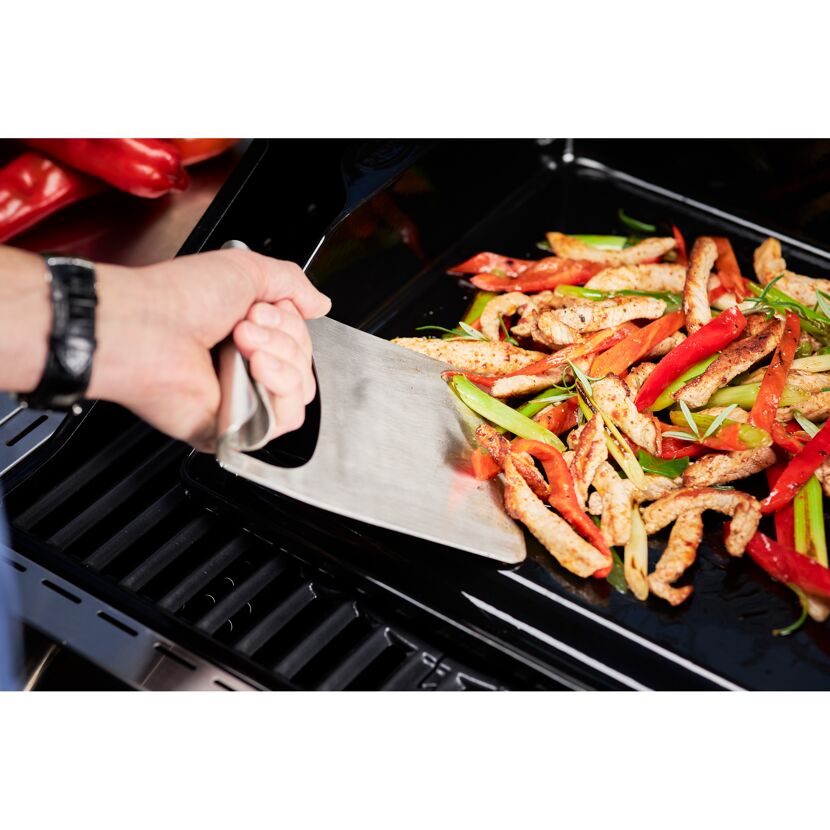 Person verwendet einen Spachtel, um Essen auf einem Grill zu wenden.