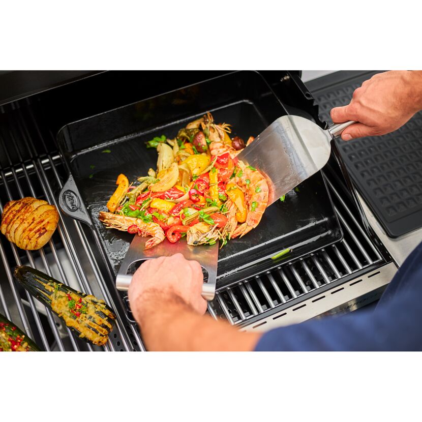 Person grillt Garnelen und Gemüse mit einem Spachtel