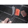 Person hält einen Grillreiniger mit orangen Borsten über einem Grillrost.