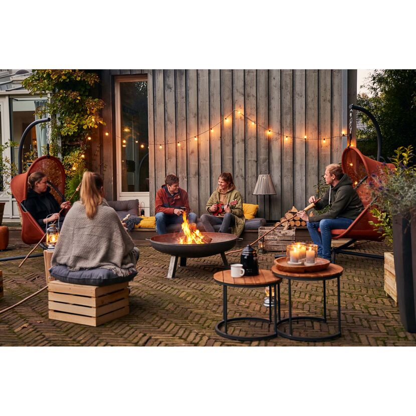 Personen sitzen um eine Feuertonne im Garten und spielen Ukulele.