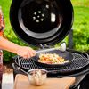 Person beim Kochen mit einem Wok auf einem Grill im Freien.