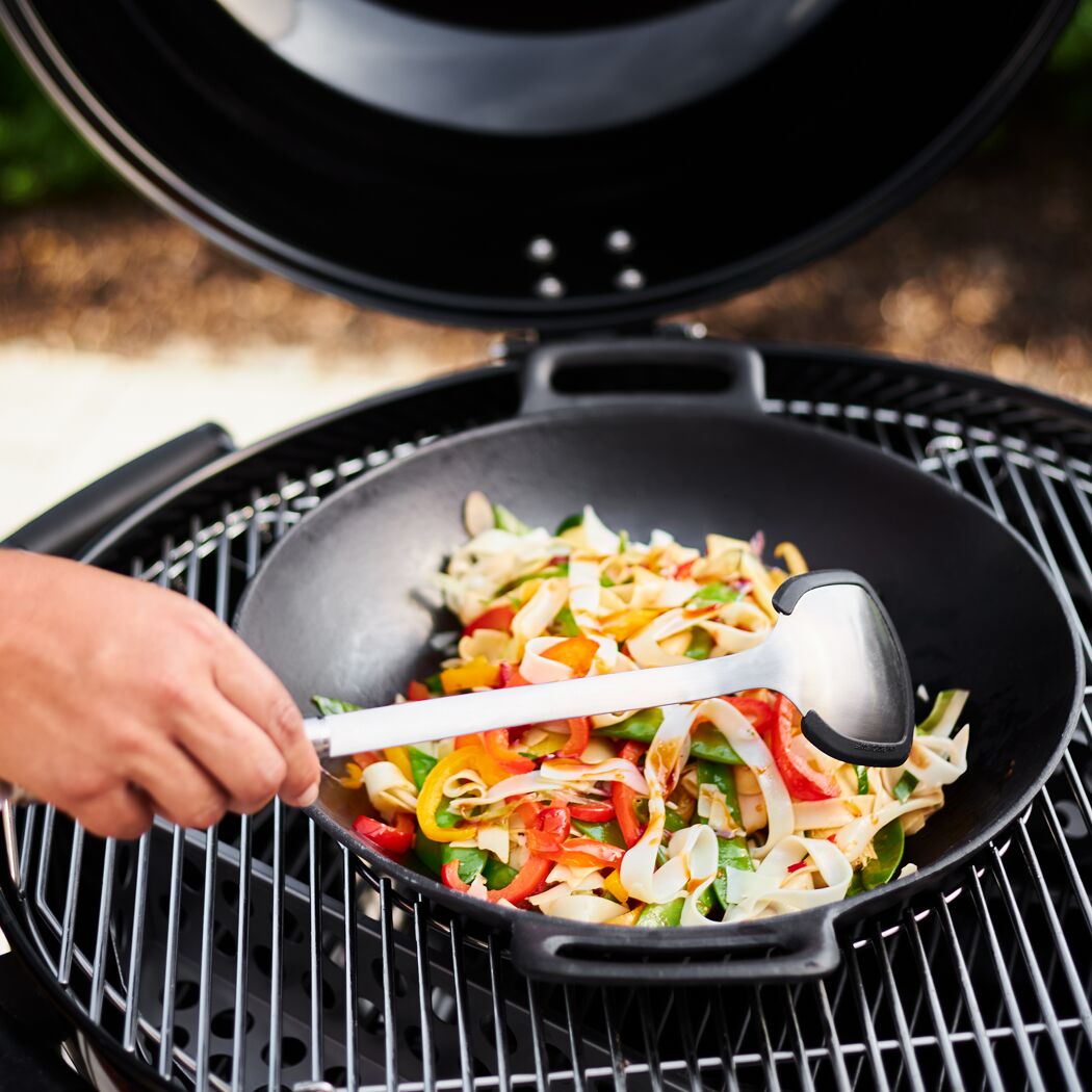 Person wendet Gemüse im Wok mit einem Woklöffel.