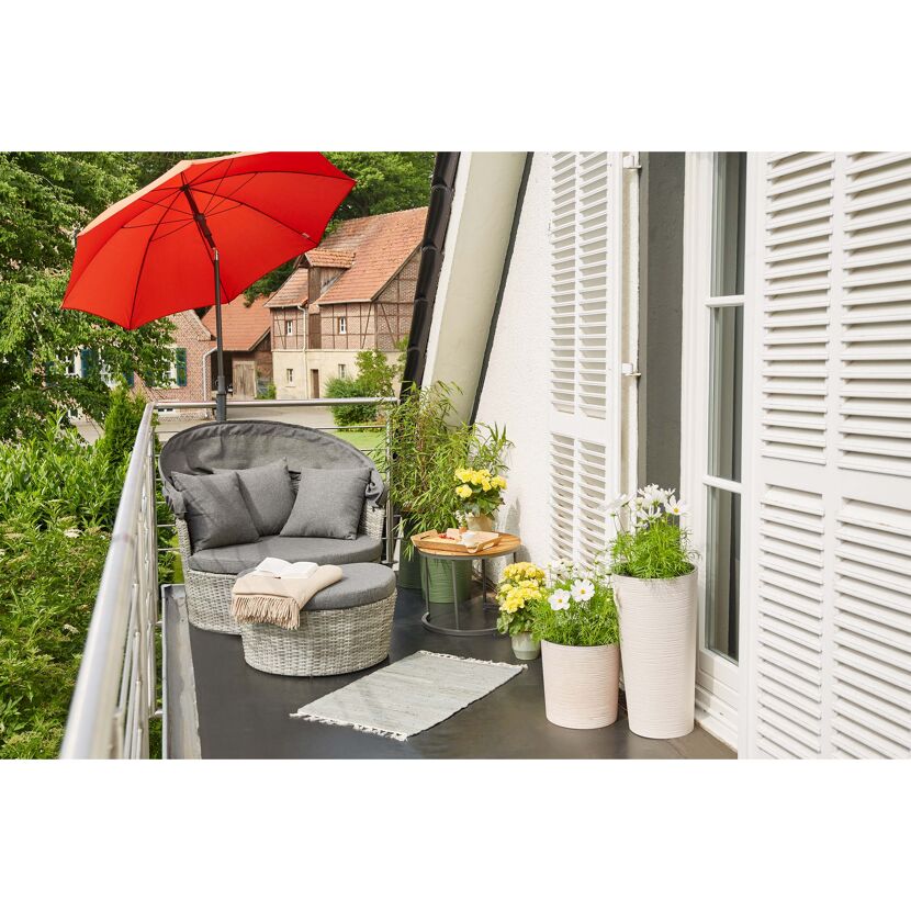 Gemütliche Loungeinsel auf einem Balkon mit rotem Sonnenschirm