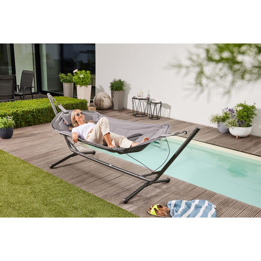 Person entspannt in einer grauen Hängematte am Pool.