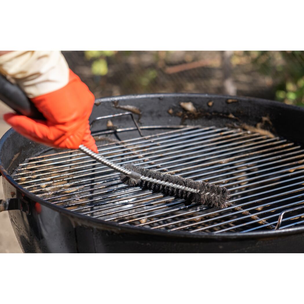 Person reinigt einen Grillrost mit einer Grillbürste.