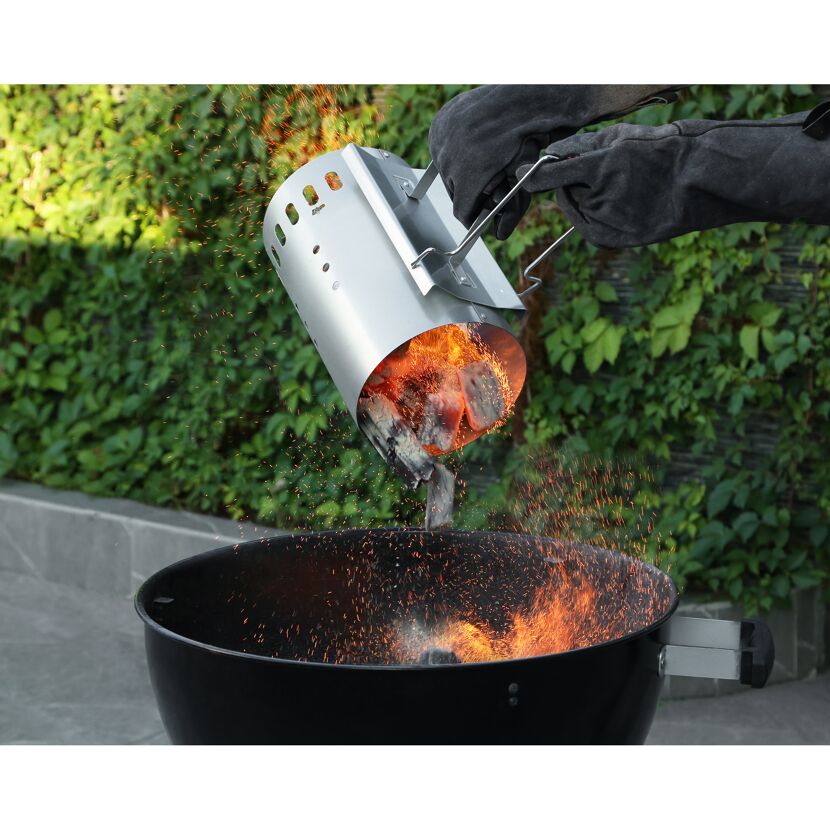 Glühende Kohlen werden mit einem Anzündkamin in einen Grill gekippt.