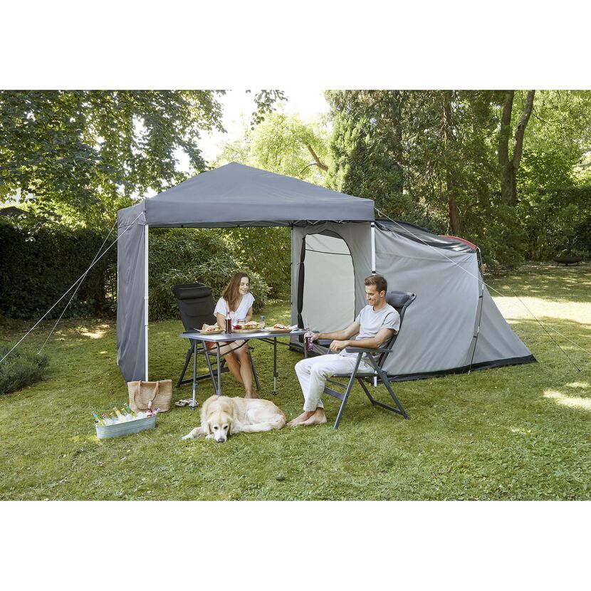 Zwei Personen sitzen im Garten mit Hund unter einem Pavillon.