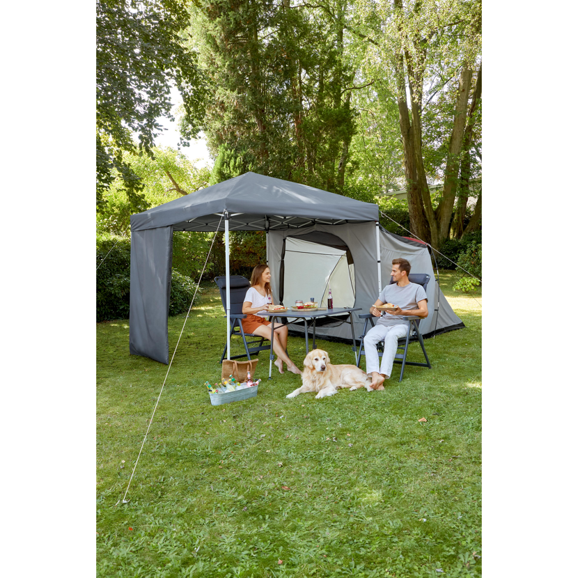 Zwei Personen sitzen an einem Tisch unter einem Pavillon und essen. Ein Hund liegt daneben.