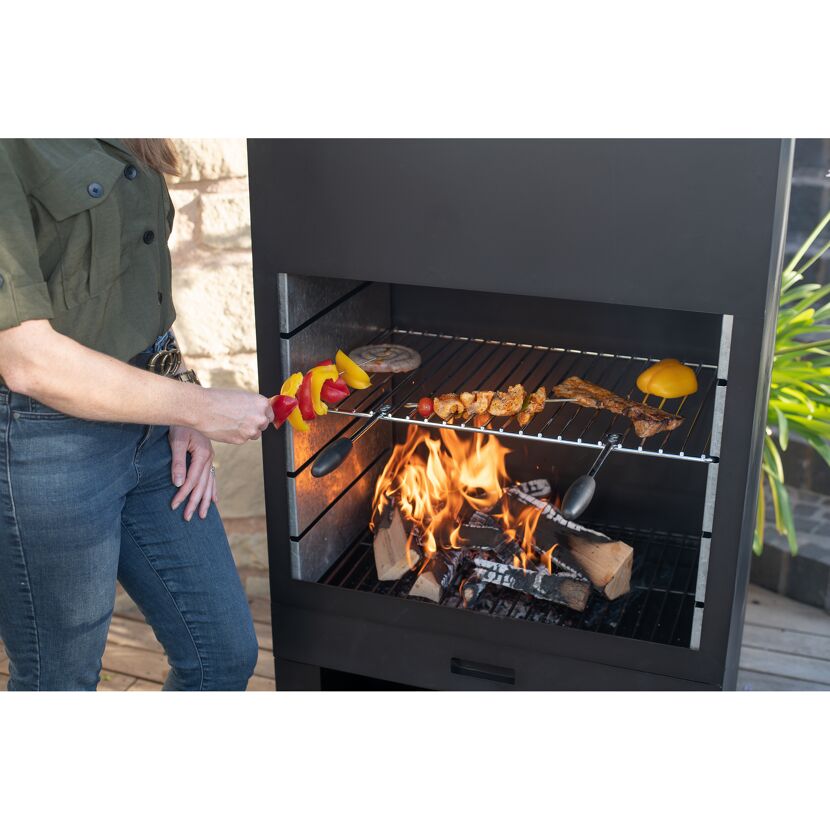 Person grillt Fleisch und Paprika auf dem Gartenkamin.