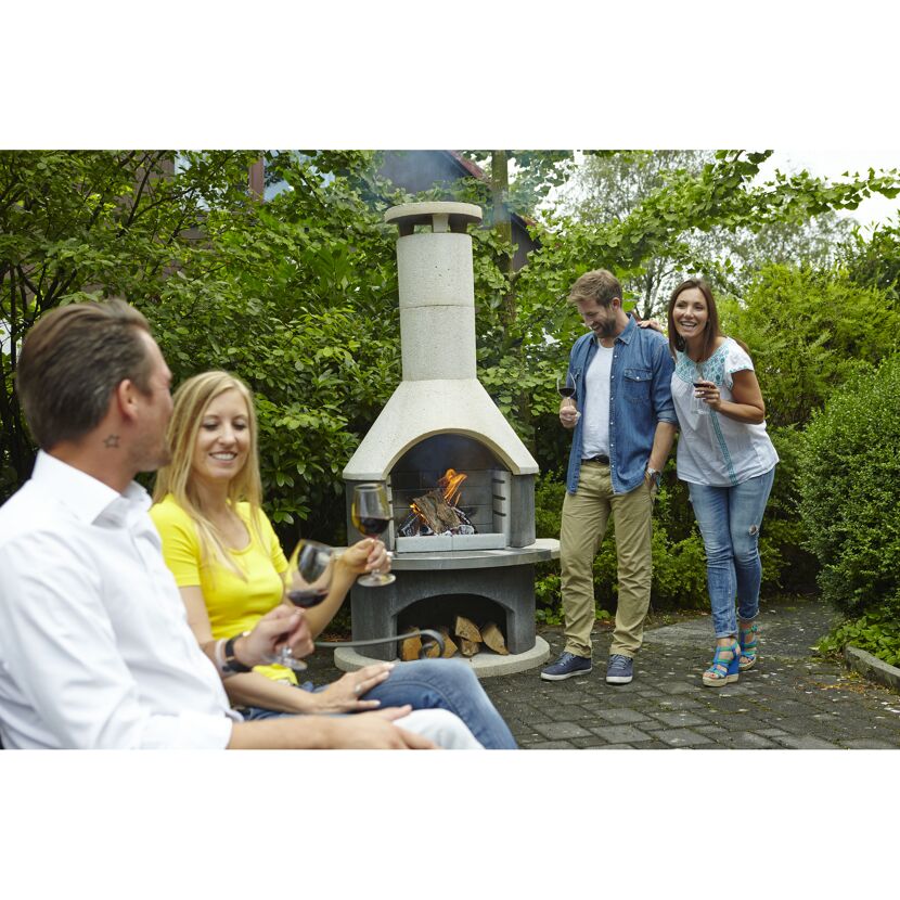 Vier Personen stoßen mit Weingläsern an einem Grillkamin an.